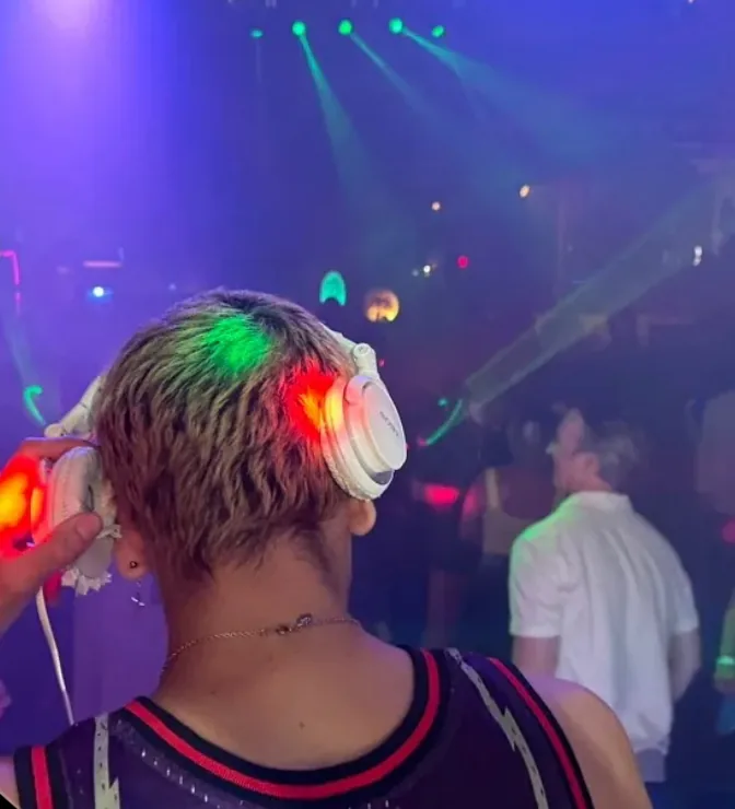 View from behind the DJ booth toward a nightclub crowd